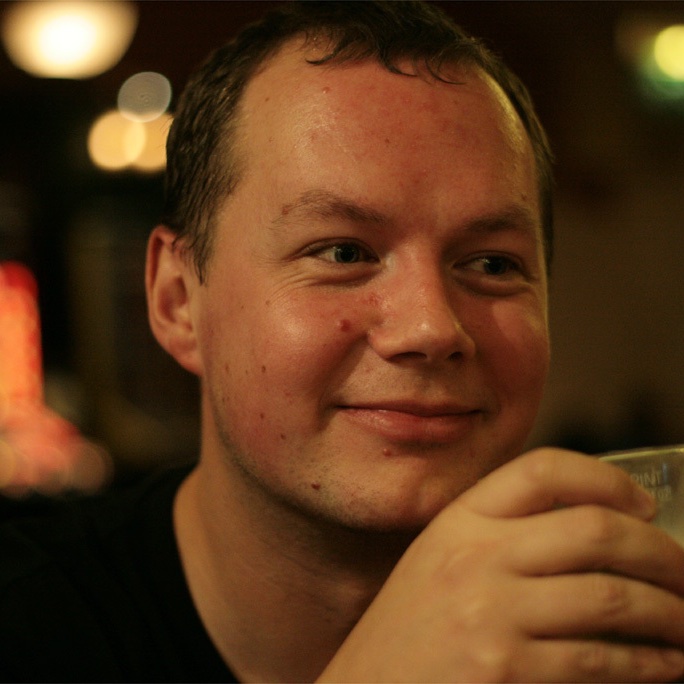 Young man with dark hair and beard, brown eyes, blue t-shirt